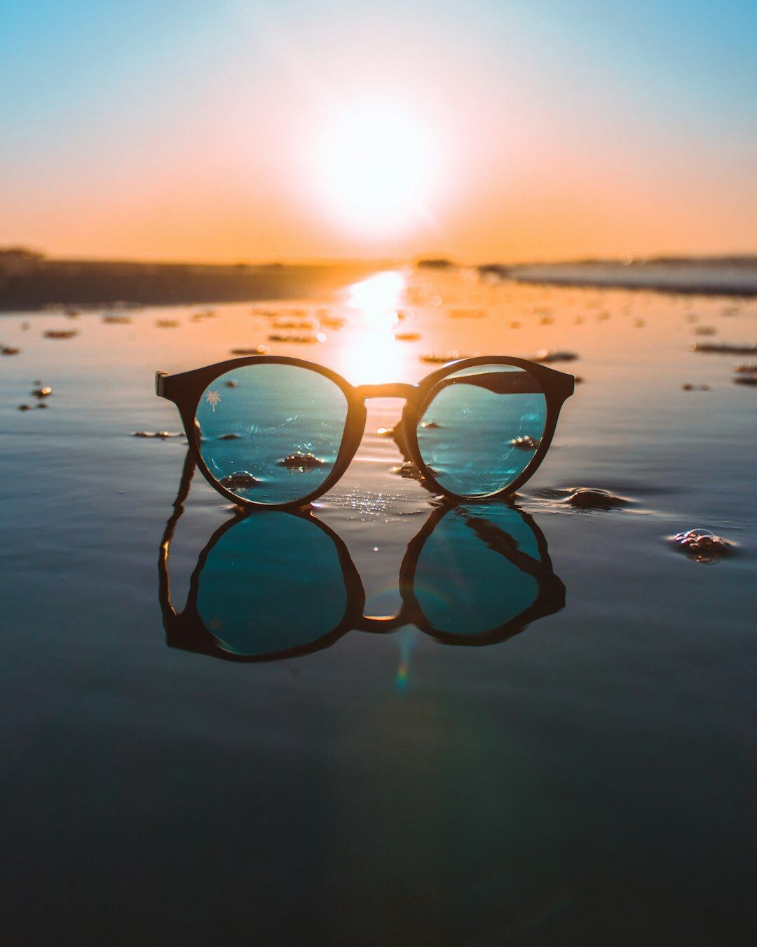 Polarized luxury sunglasses resting on white sand with the Atlantic coast of Uruguay in the background